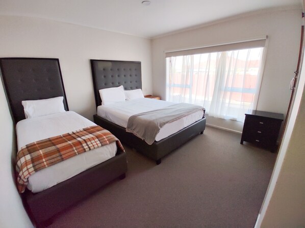 A hotel room with two beds, a large window with sheer curtains, and a small dark dresser. - 136 St George Motel (Auckland)