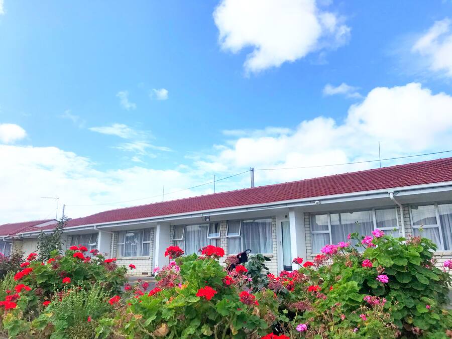 A row of white buildings with red roofs, surrounded by lush greenery and vibrant flowers.
