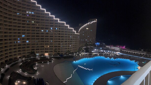 Un hotel grande con varios pisos, un patio central con piscina y zonas ajardinadas alrededor.