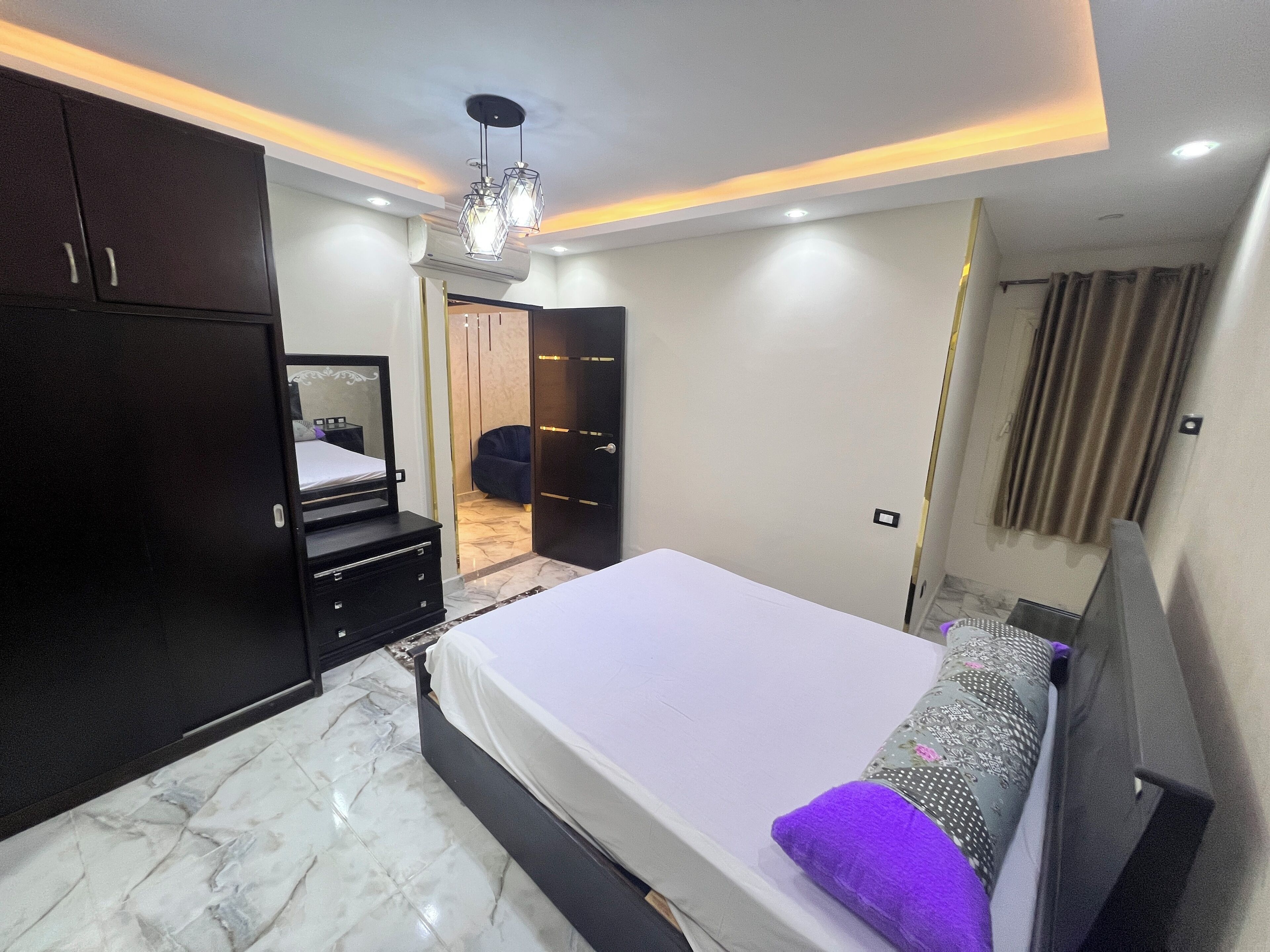 Un dormitorio moderno con una cama grande, un armario de madera oscura y una lámpara en el techo.