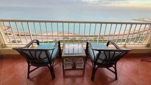 Un balcón con dos sillas de mimbre y una mesa pequeña, con vistas a la costa y un cielo despejado.