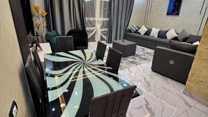 Una sala de estar moderna con una mesa de comedor de vidrio, sofás oscuros y piso de mármol.