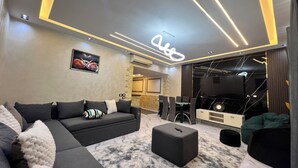 Una sala de estar moderna con un sofá gris, un taburete negro, un tapiz con estampado de mármol y un televisor al fondo.