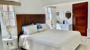 A bedroom with a bed, bedside table, lamp, dresser, mirror, and a wooden door.