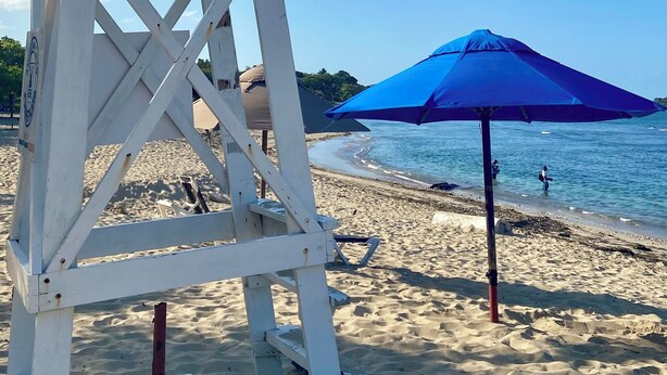 A lifeguard tower and a blue umbrella on a sandy beach.