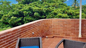 A patio with two wicker chairs with blue cushions, a brick wall, and a view of green trees and the sky.