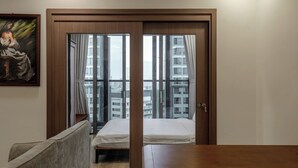 A hotel room with a bed, a wooden desk, a chair, and a large window with curtains.