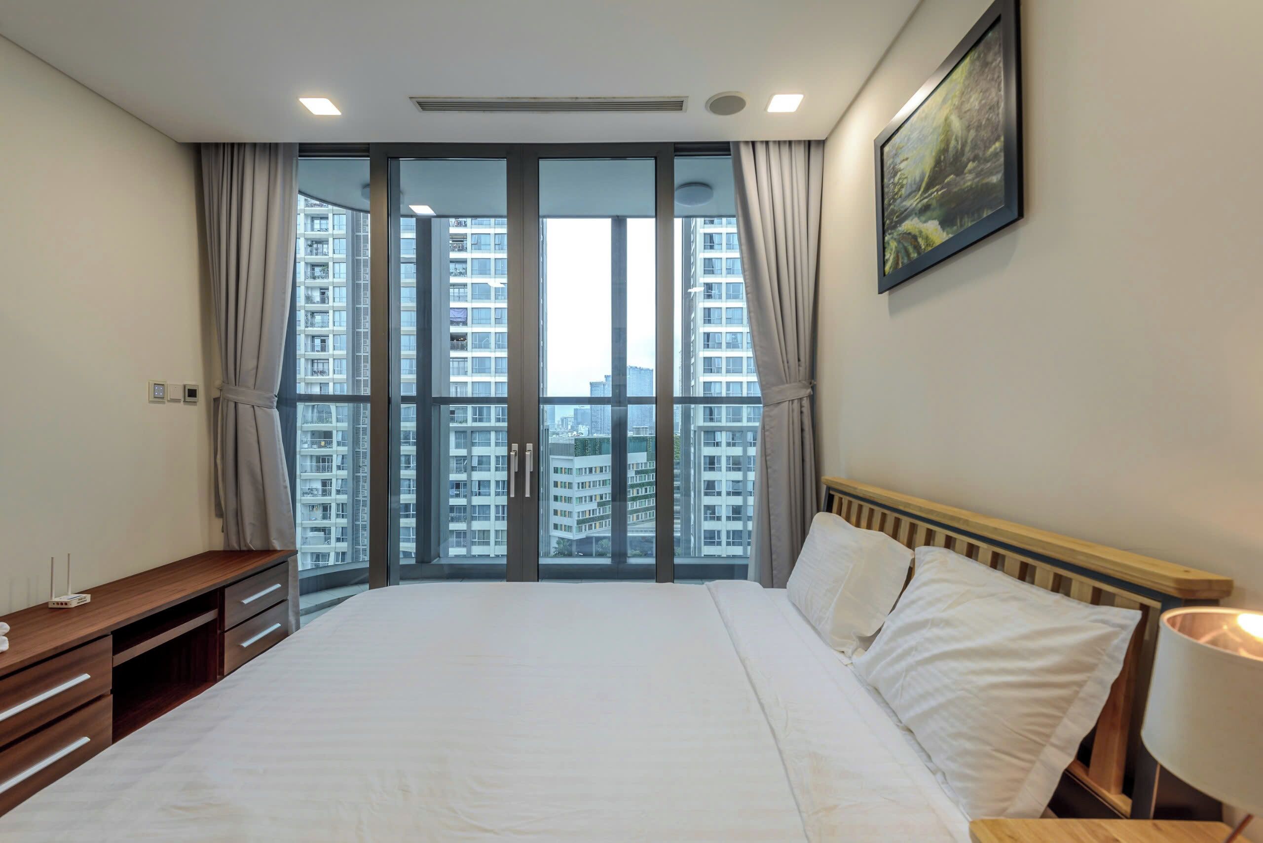 Een hotelkamer met een groot bed, een houten bureau en een uitzicht op wolkenkrabbers door raam-tot-plafond ramen.
