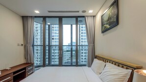 A hotel room with a large bed, a wooden desk, and a view of high-rise buildings through floor-to-ceiling windows.