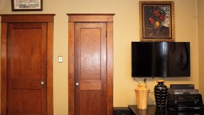 Una stanza con due porte in legno, una TV a schermo piatto montata al muro, un vaso di legno e un altoparlante nero su un tavolo in legno.