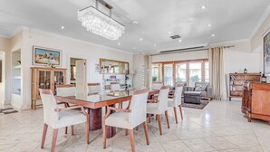 A spacious living room with a large dining table, comfortable seating, a chandelier, and a view of the outdoors. - House Sunbeam GuestHouse (Johannesburg)