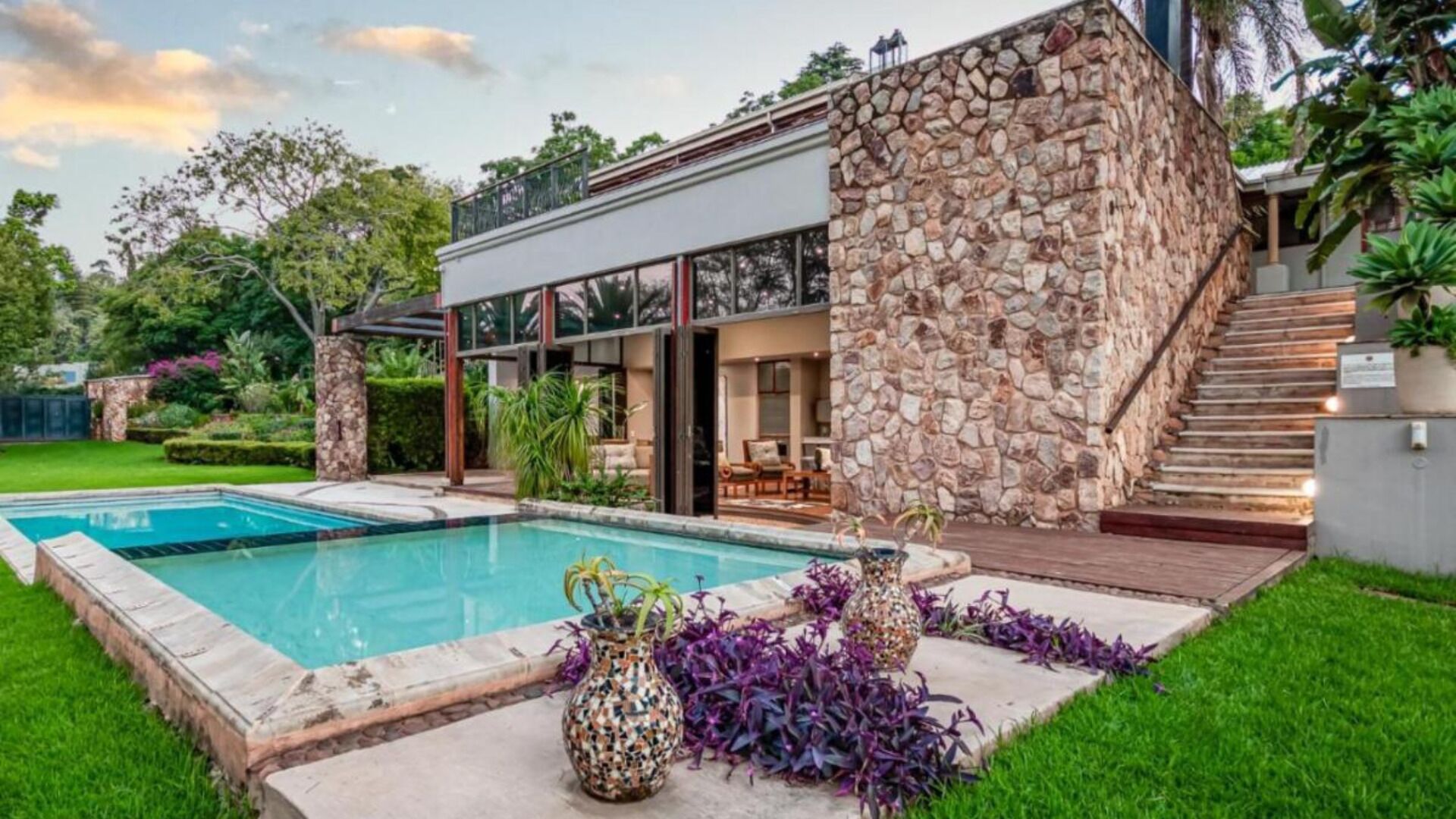 A modern house with a stone exterior, a swimming pool, and a well-maintained garden.
