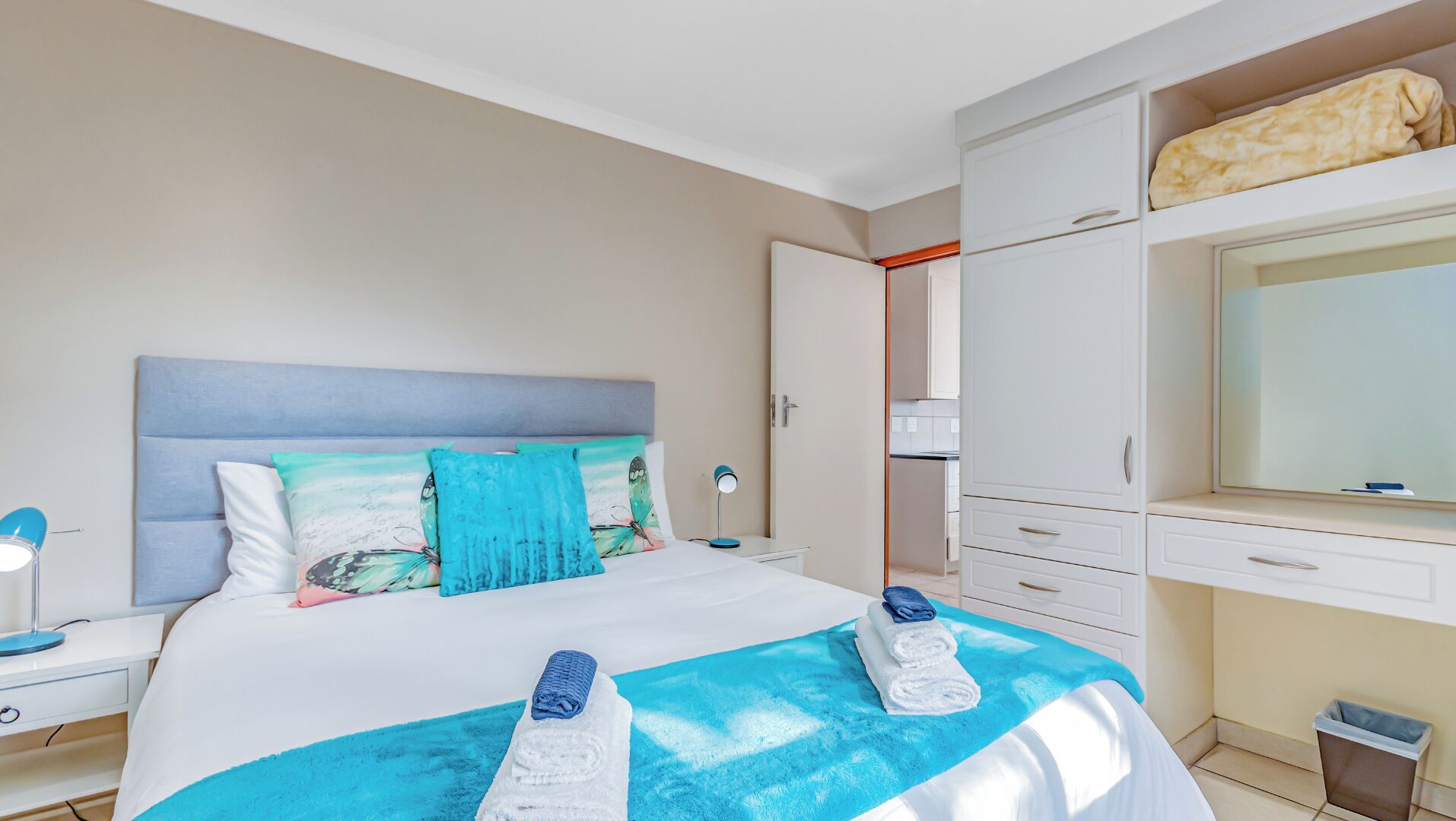 A hotel room with a bed, a nightstand, a desk, a wardrobe, and a mirror.