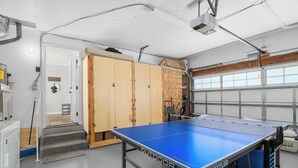 Une table de ping-pong dans un garage, avec une armoire en bois et une fenêtre.
