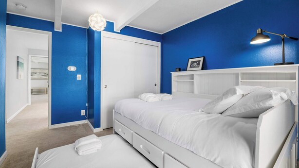 Une chambre avec un lit blanc, une commode blanche et un mur d’accent bleu.