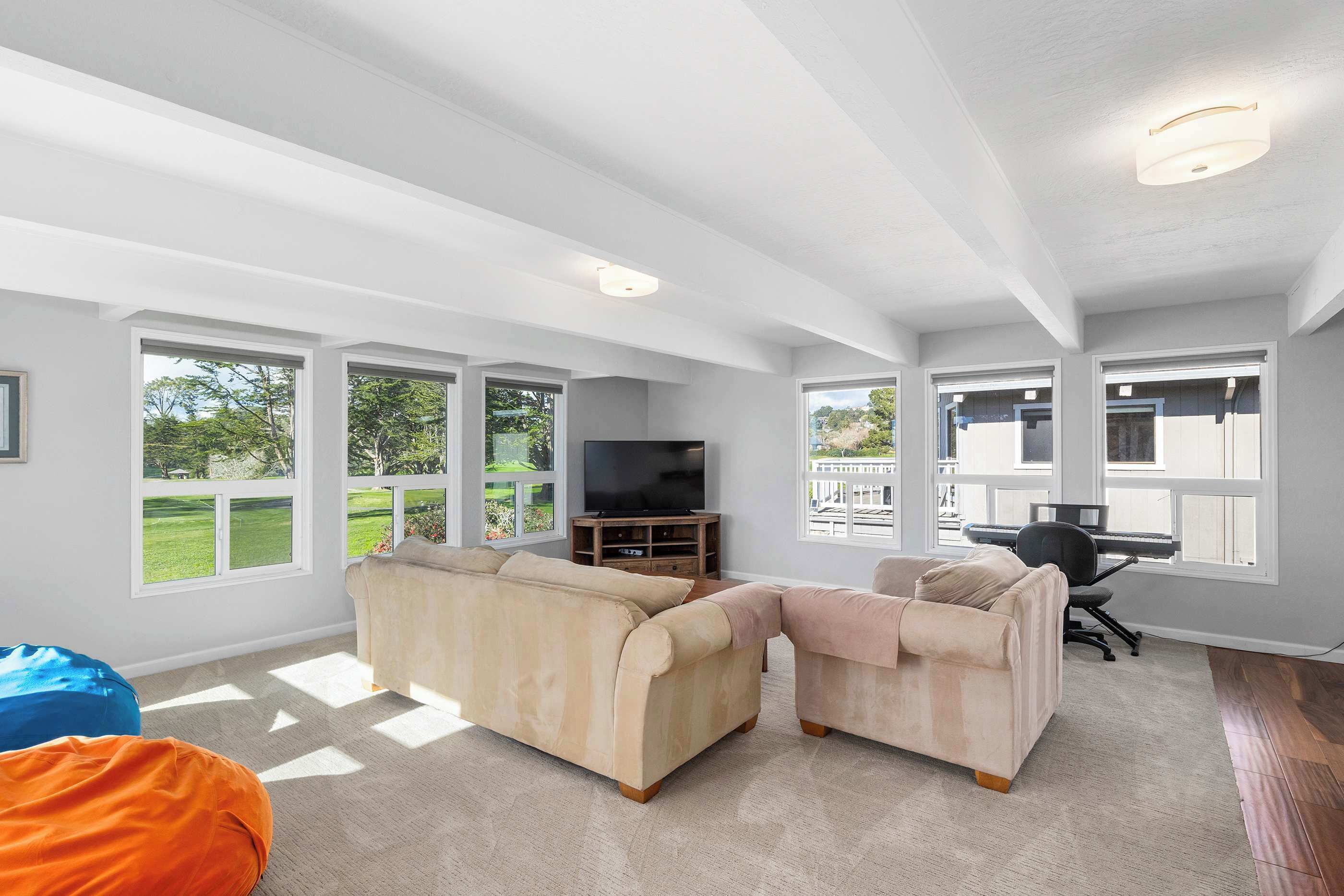 A spacious living room with large windows, a flat-screen TV, and a piano.