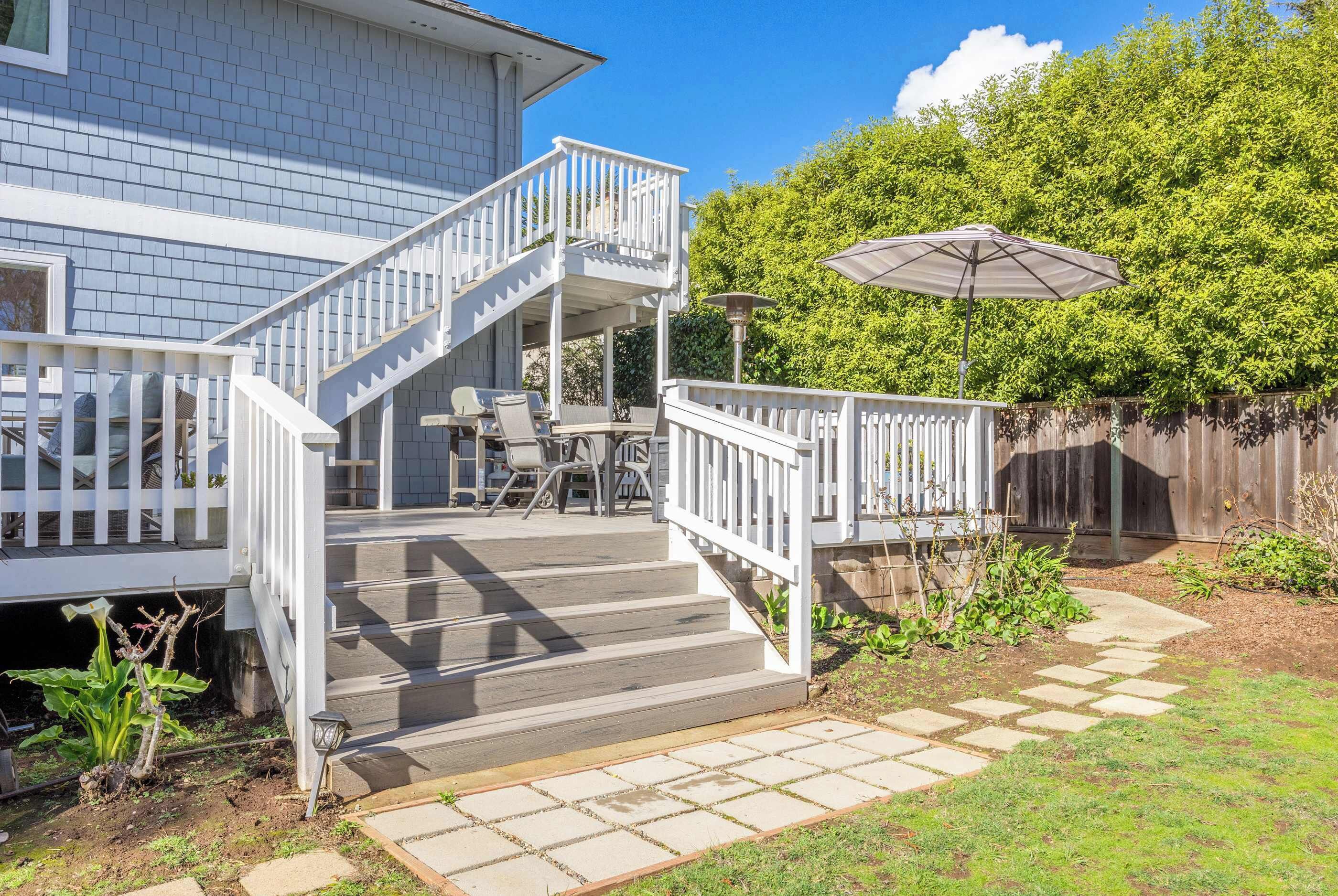 A two-story house with a covered patio area, outdoor furniture, and a wooden fence.