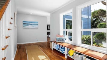 A hallway with wooden flooring, a bench with storage, a painting, and a window with a view of the outside.