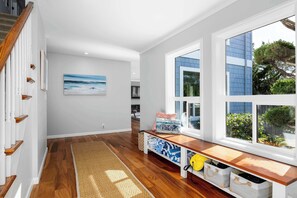 A hallway with wooden flooring, a bench with storage, a painting, and a window with a view of the outside.