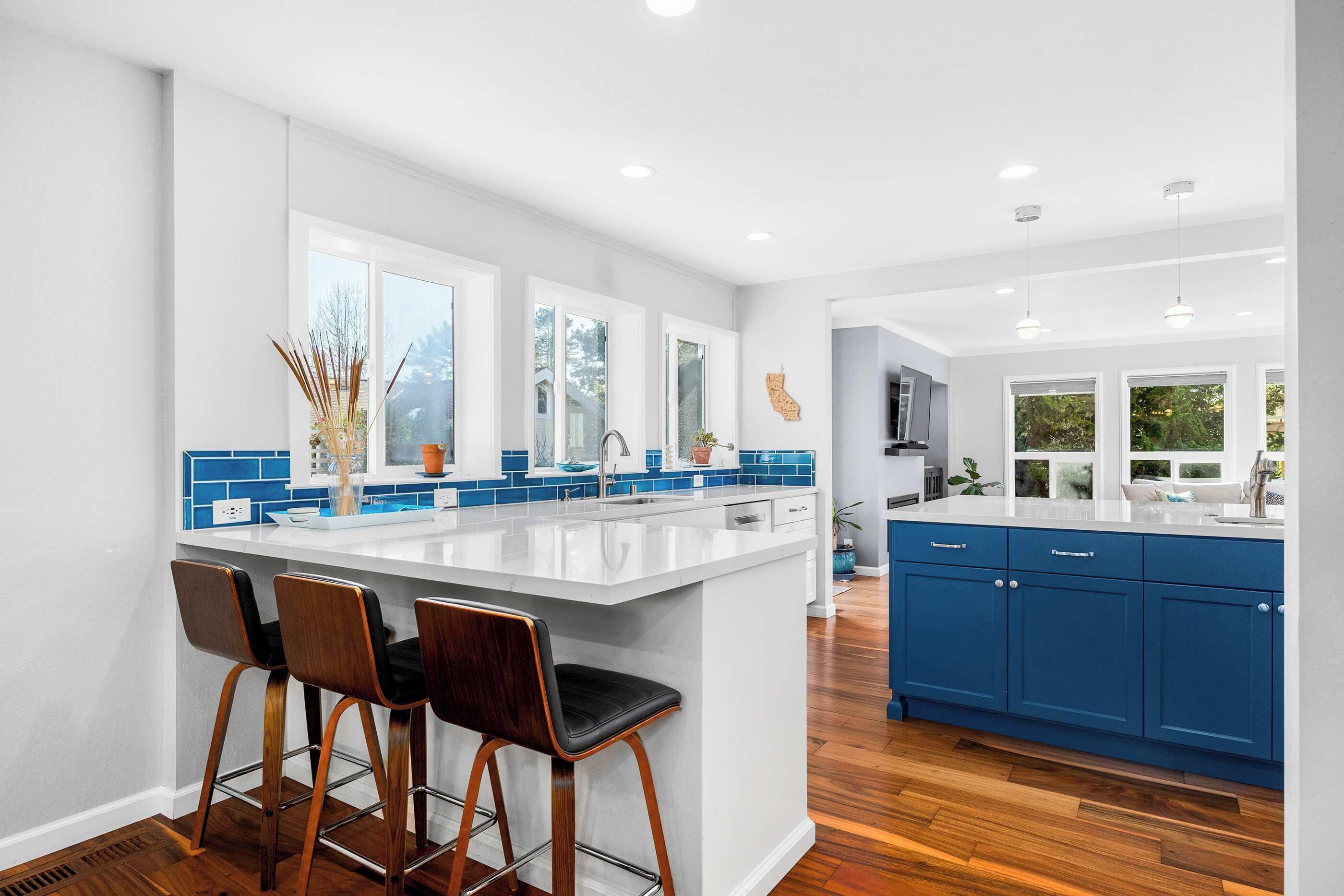 A modern kitchen with a large island, bar stools, and blue cabinets.