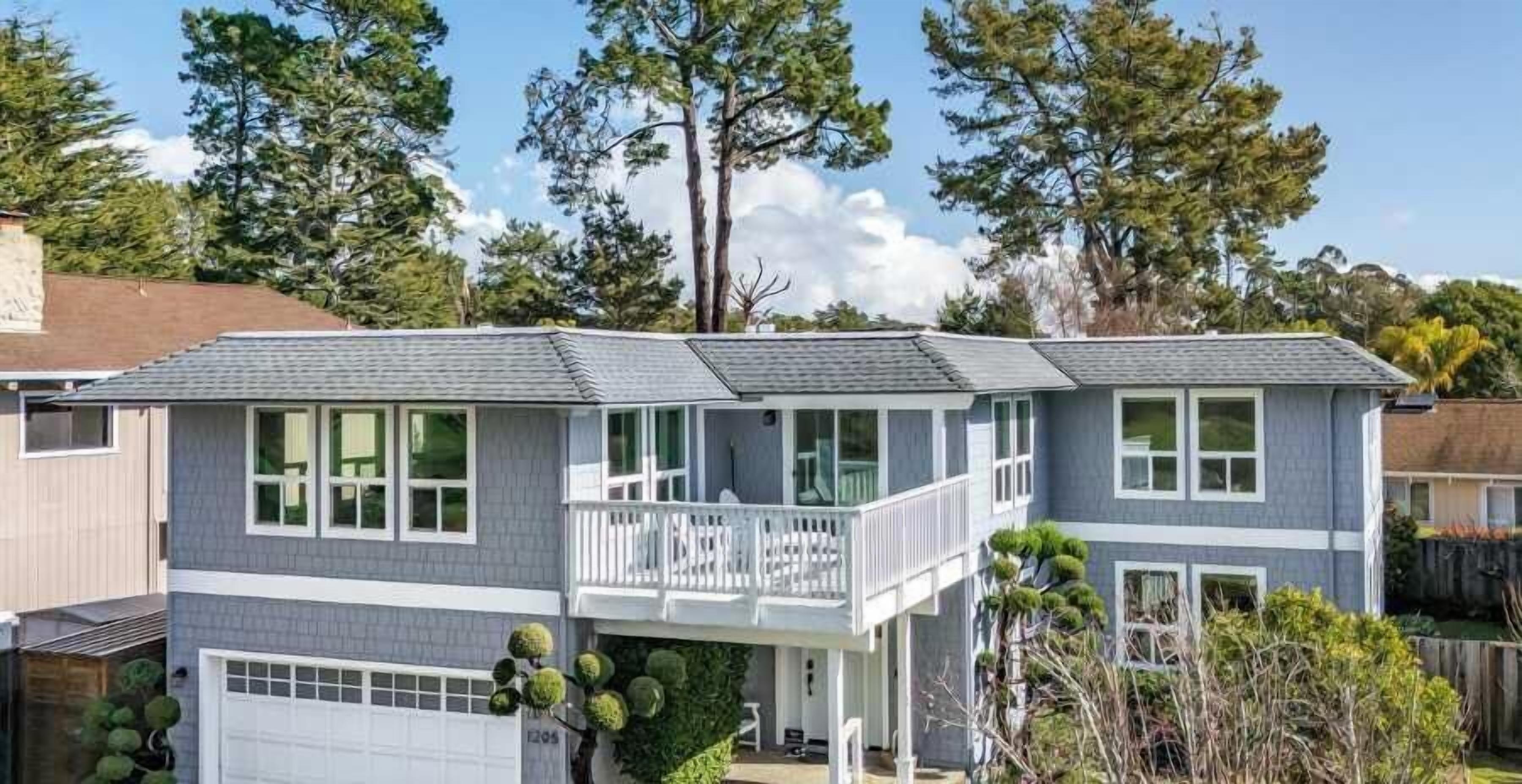 A two-story residential building with a balcony on the upper floor, a garage, and a well-maintained garden.