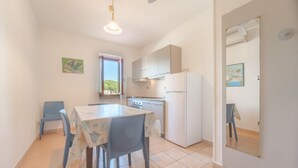 A compact kitchen with a dining table, chairs, a refrigerator, and a window. - APPARTAMENTI GLI ORIZZONTI - ORIZZONTI BILO 4 (Campo nell'Elba)