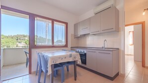 A small kitchen with a dining table and chairs, a window with curtains, and an air conditioning unit.