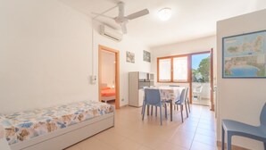 Een kleine, lichte kamer met een bed, een tafel met stoelen en een kitchenette.