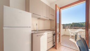 A compact kitchen with a refrigerator, sink, and cabinets, leading to a balcony with a table and chairs.