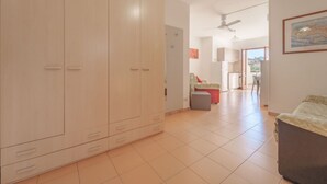 A spacious room with a large wardrobe, a dining area with a table and chairs, and a kitchen visible through an open doorway.