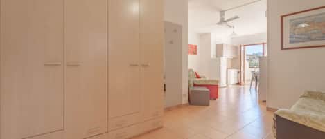 A spacious room with a large wardrobe, a dining area with a table and chairs, and a kitchen visible through an open doorway.