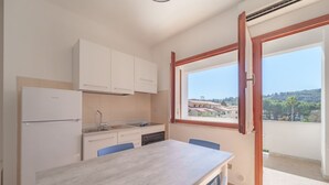 A compact kitchen with a dining area, a built-in refrigerator, and a window offering a view of the surrounding area. - APPARTAMENTI GLI ORIZZONTI - ORIZZONTI MONO 22 (Marina di Campo)