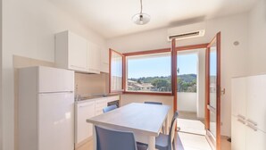 A compact kitchen with a dining area, white cabinets, a built-in oven, and a large window offering a view of a hillside. - APPARTAMENTI GLI ORIZZONTI - ORIZZONTI MONO 22 (Marina di Campo)