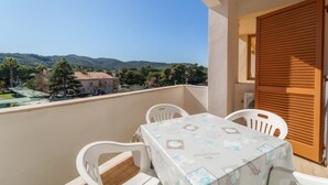 A balcony with a table and chairs, overlooking a scenic view of hills and buildings. - APPARTAMENTI GLI ORIZZONTI - ORIZZONTI MONO 22 (Marina di Campo)