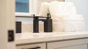 Een badkamer met een wit marmeren aanrecht, een zwarte zeepdispenser en een witte handdoekmand.