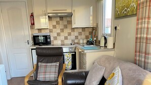 Een ruimtelijk ingerichte zithoek met kitchenette, een bank, een fauteuil en vloerkleed.
