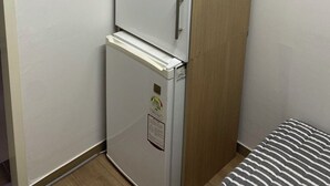 Une pièce de taille modeste, comprenant un petit réfrigérateur blanc, une armoire en bois et un lit avec une literie à rayures.