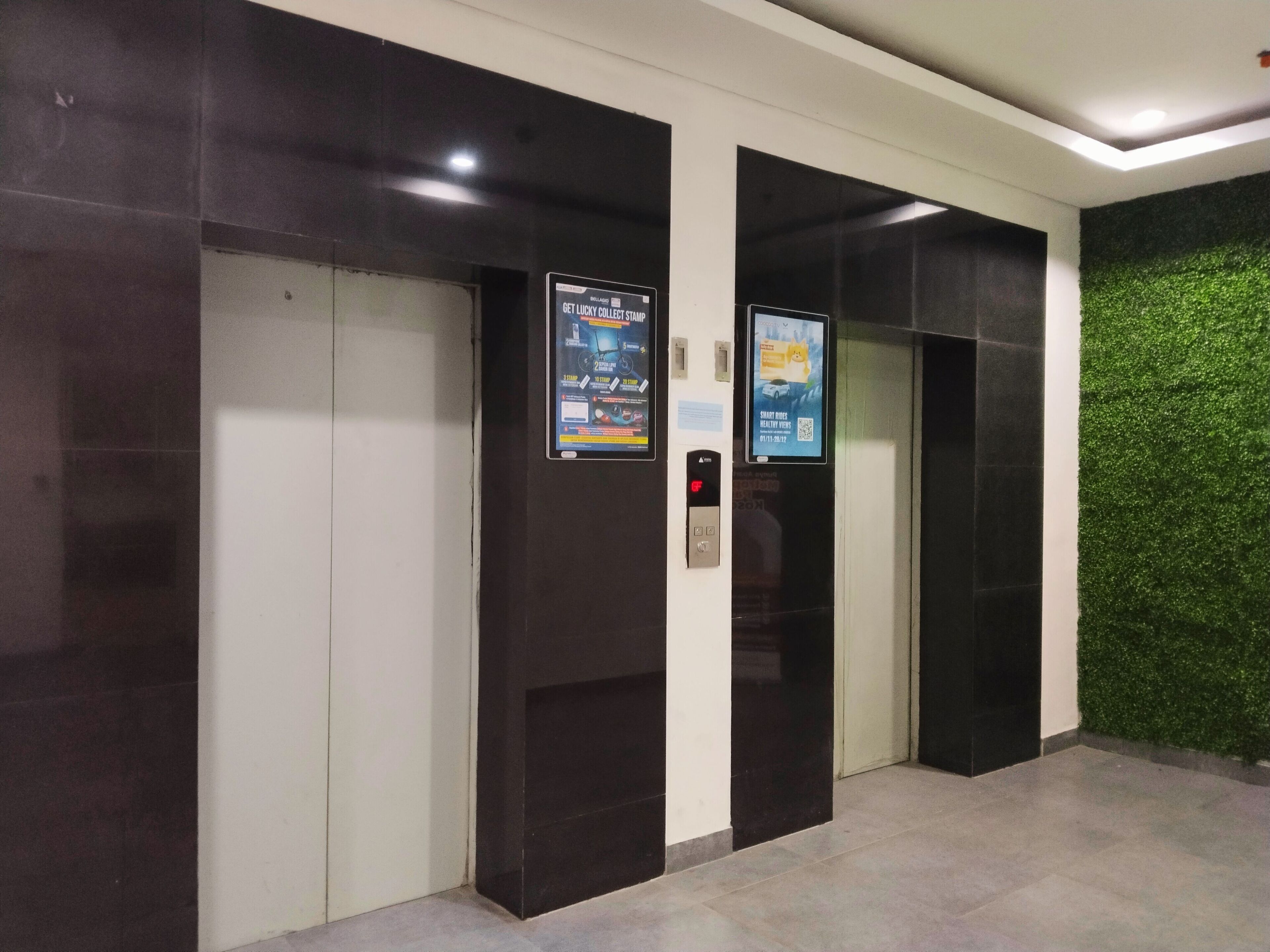 Two elevator doors with digital displays and a green wall.