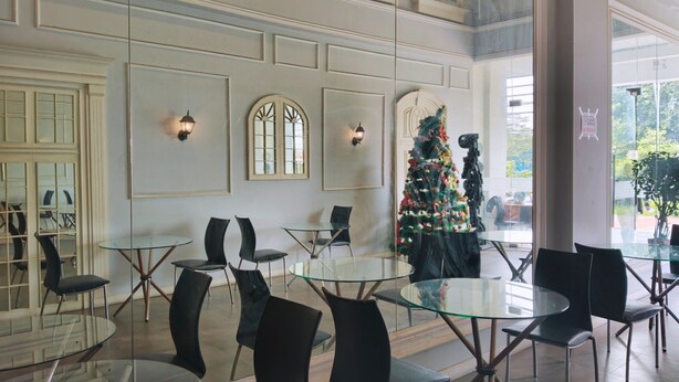 Ein moderner Essbereich mit Glastischen und schwarzen Stühlen, ein geschmückter Weihnachtsbaum und Blick ins Freie.