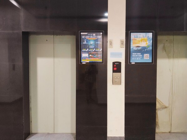 An elevator with two digital displays advertising a stamp collection and a car rental service.
