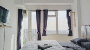 Ein Schlafzimmer mit einem Bett, einem an der Wand montierten Fernseher und einem Fenster mit Vorhängen.
