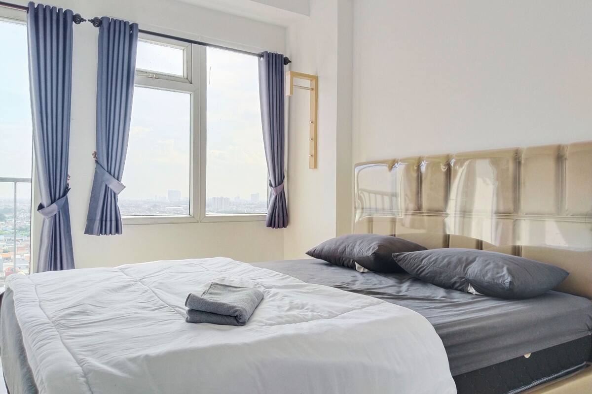 A hotel room with a bed, a window with curtains, and a city view.
