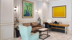 Ein modernes Wohnzimmer mit einer Couch, einem Couchtisch und einem Schreibtisch mit einem Computer. Zwei Wandlampen und ein Baumgemälde sind ebenfalls vorhanden.