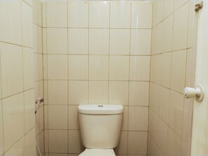 A small, enclosed bathroom with a toilet, tiled walls, and a door. - Amerta Room Metropolitan Park powered by Cocotel (Bekasi)