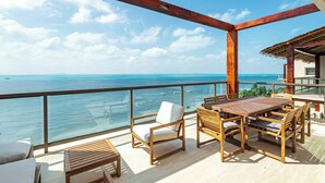 Terraza de madera con mesa y sillas, con vista a un mar azul y despejado.