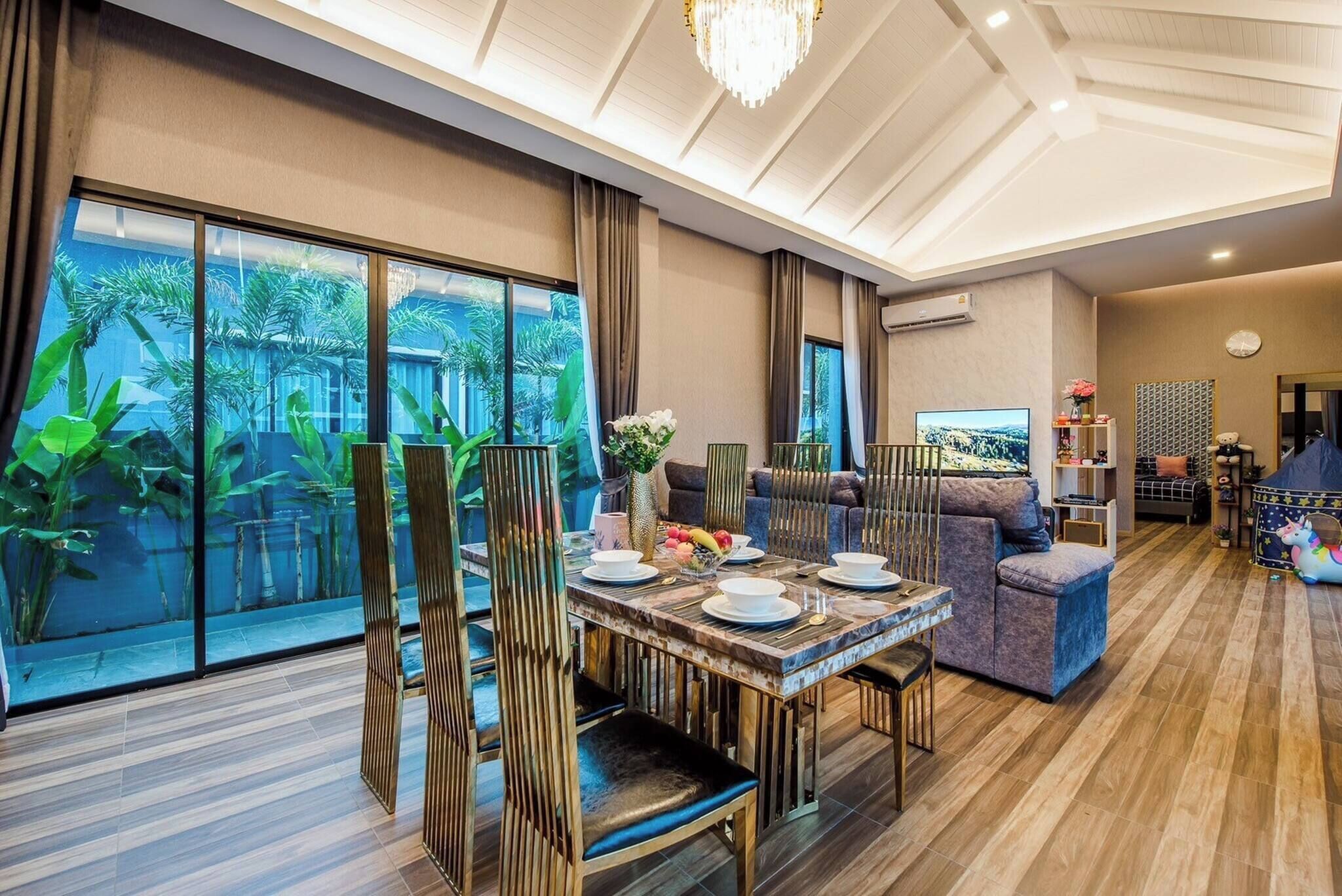 A modern living room with a dining area, large windows, and a chandelier.