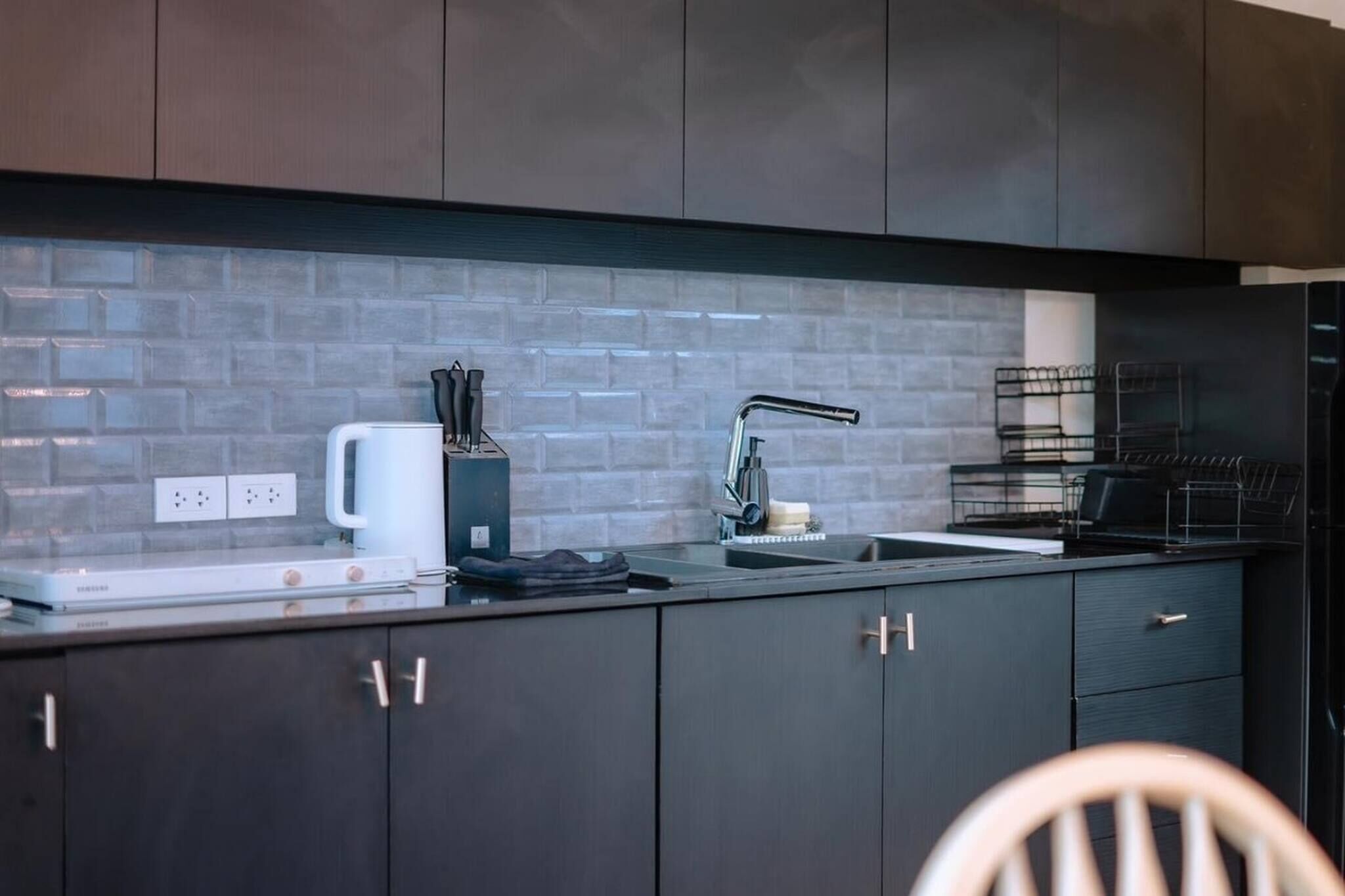 A modern kitchen with dark cabinetry, a white countertop, and a tiled backsplash.