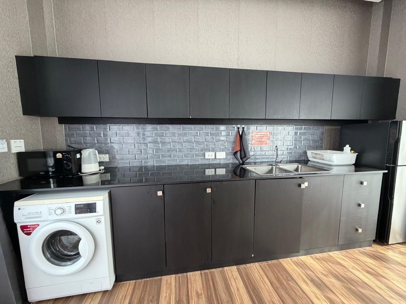 Una cocina compacta con armarios oscuros, microondas integrado, cafetera y lavadora.