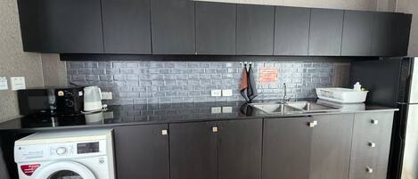 Una cocina compacta con armarios oscuros, microondas integrado, cafetera y lavadora.