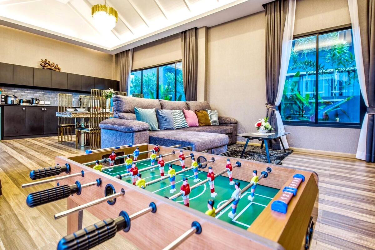Une pièce comprenant une table de baby-foot, un canapé, une table à manger et un coin cuisine.